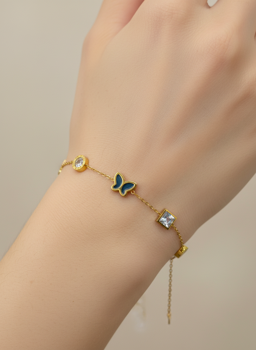 Gold bracelet with a butterfly charm on a wrist against a neutral background