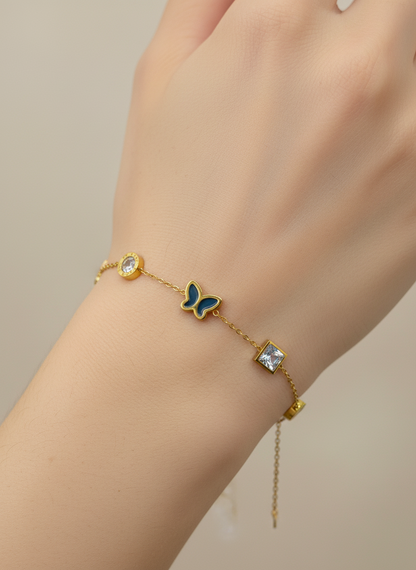 Gold bracelet with a butterfly charm on a wrist against a neutral background