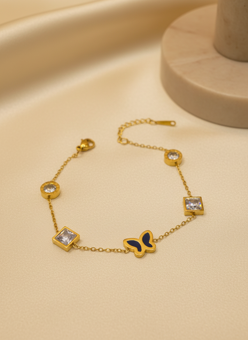 Gold bracelet with butterfly and gemstone details on a beige surface