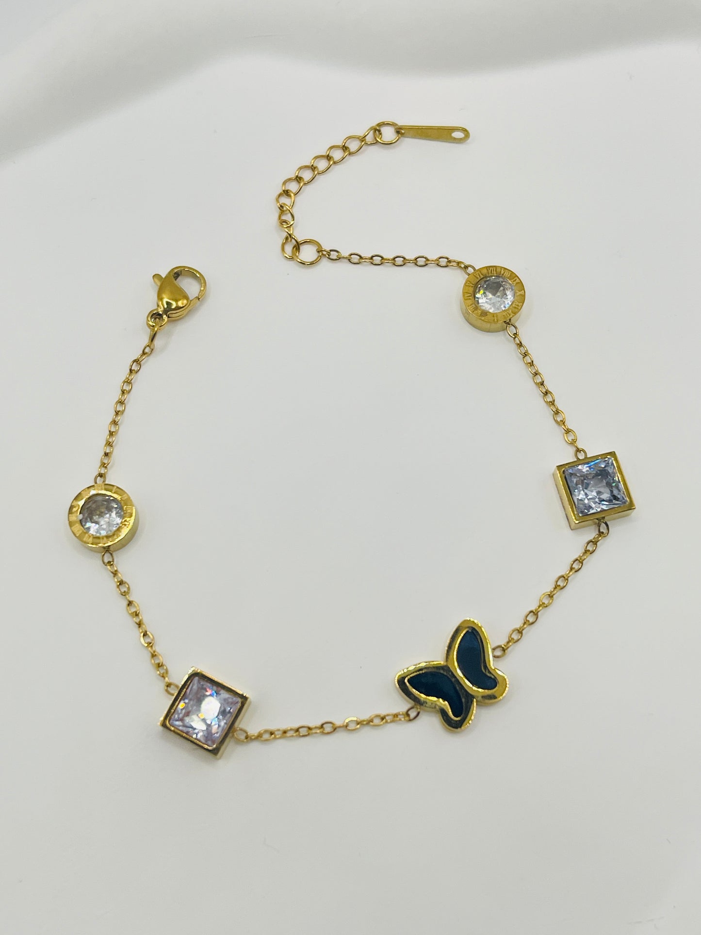 Gold bracelet with butterfly and gemstone charms on a white background