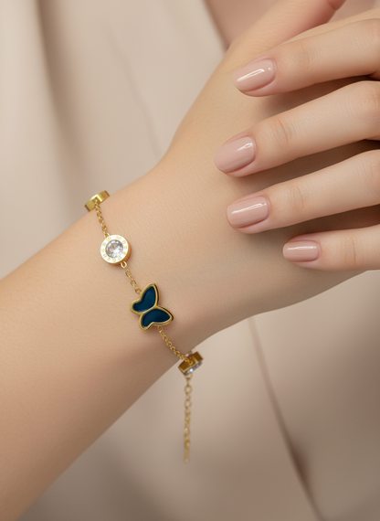 Gold bracelet with a blue butterfly charm on a wrist against a beige background