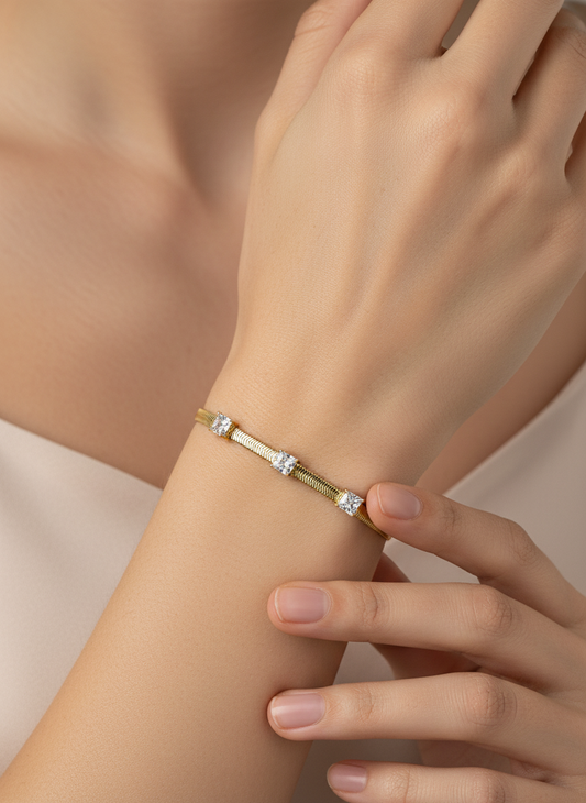 Gold bracelet with diamond-like stones on a light gray background