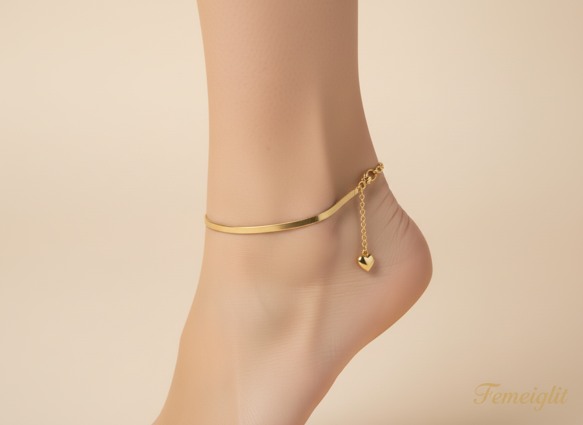 Gold anklet with a heart-shaped charm on a foot against a beige background