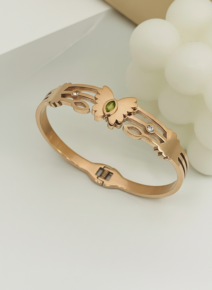 Rose gold bracelet with a green gemstone on a light background