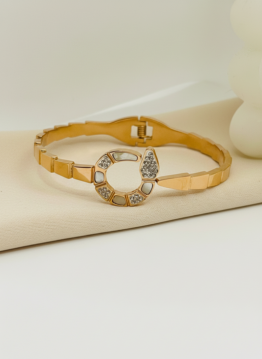 Gold bracelet with a decorative clasp on a beige surface