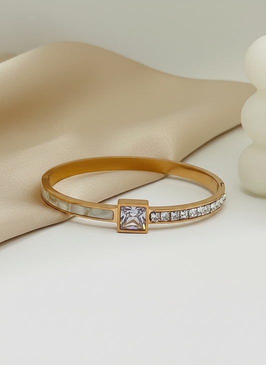 Rose Gold bracelet with a square gemstone and smaller stones on a beige fabric background