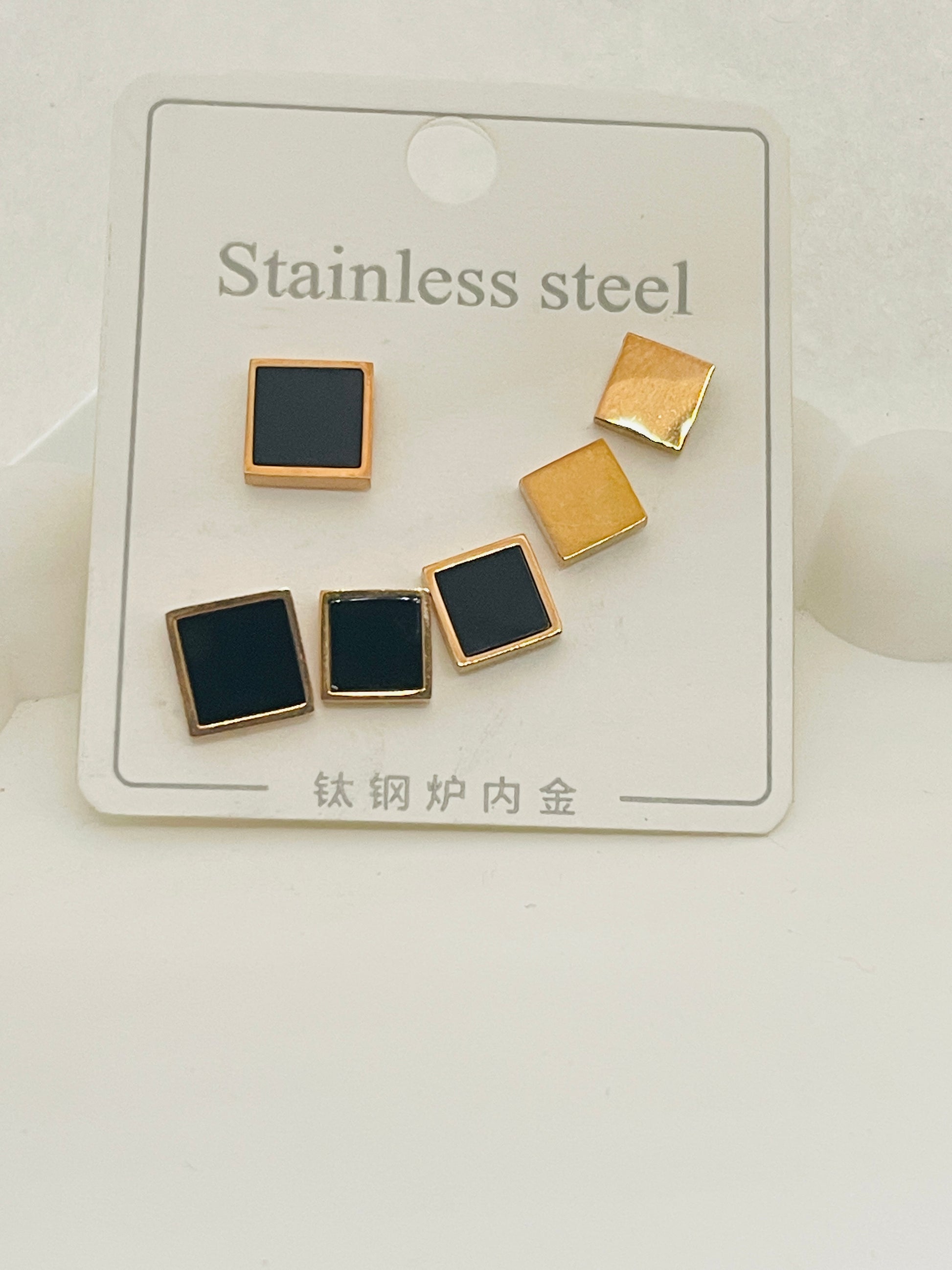 Pair of square-shaped earrings with gold and black finishes on a white card.