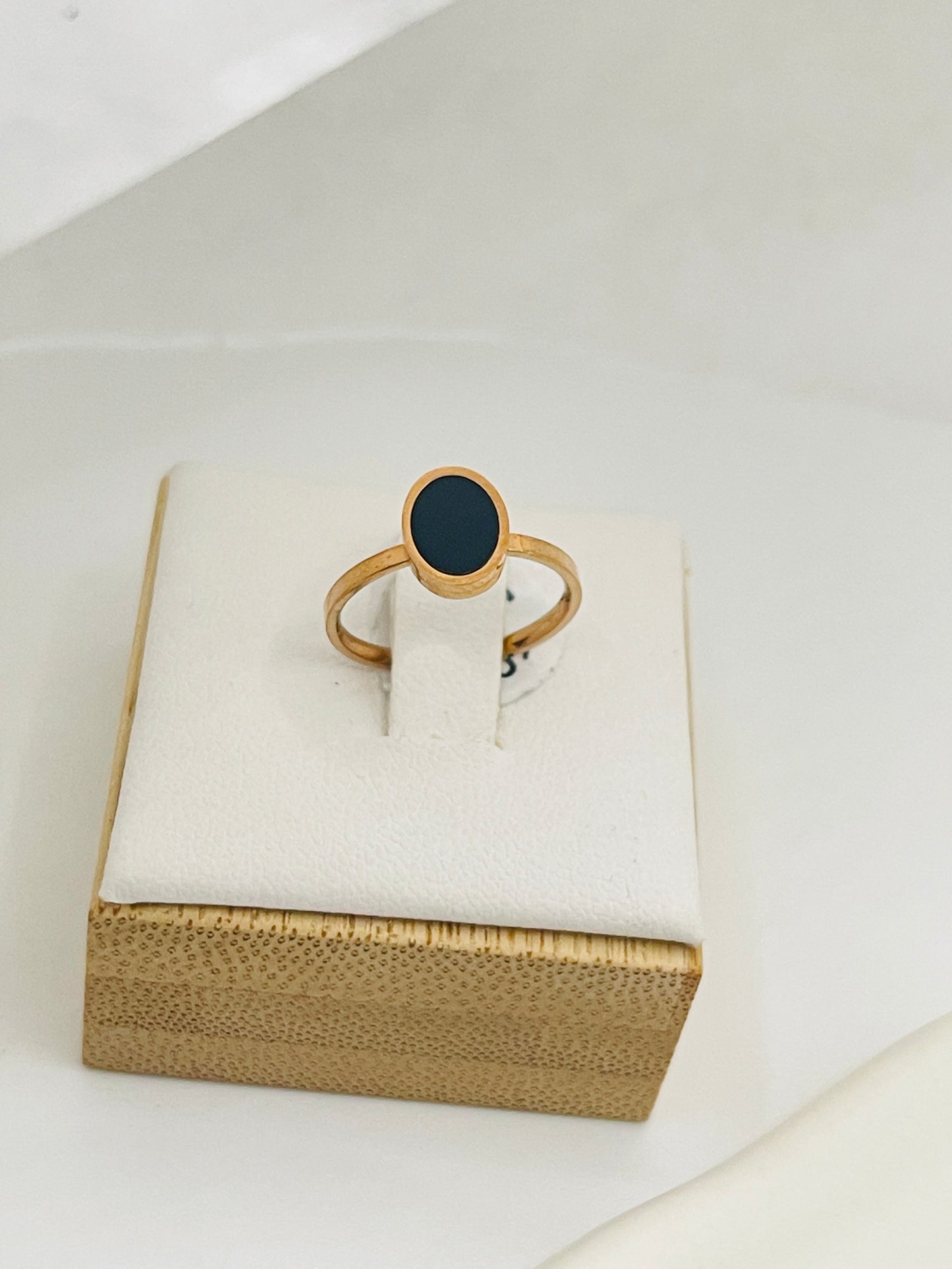 Rose Gold ring with a black stone on a white cushion inside a gold box.