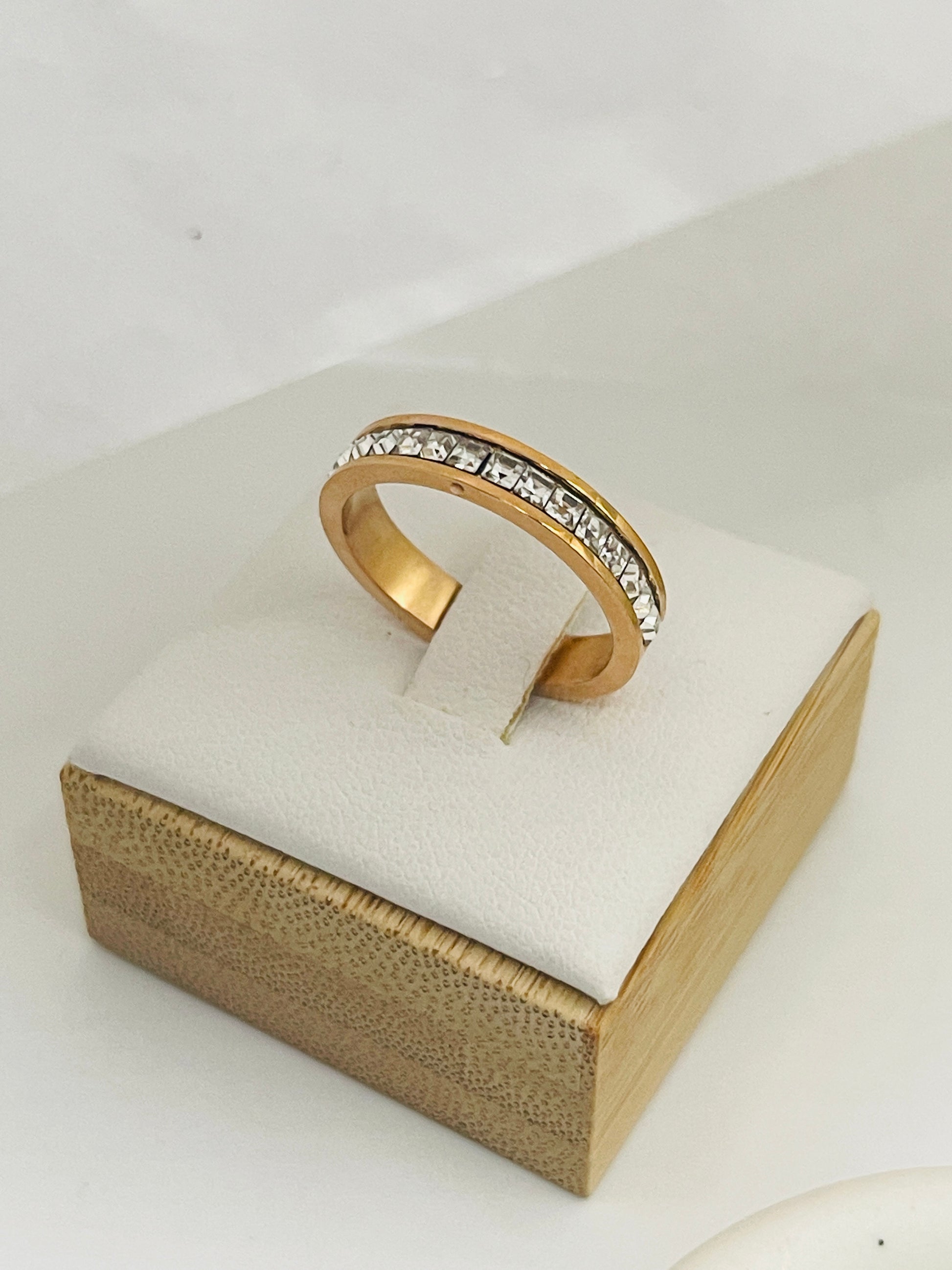 Rose Gold ring with embedded stones on a white cushion in a gold box