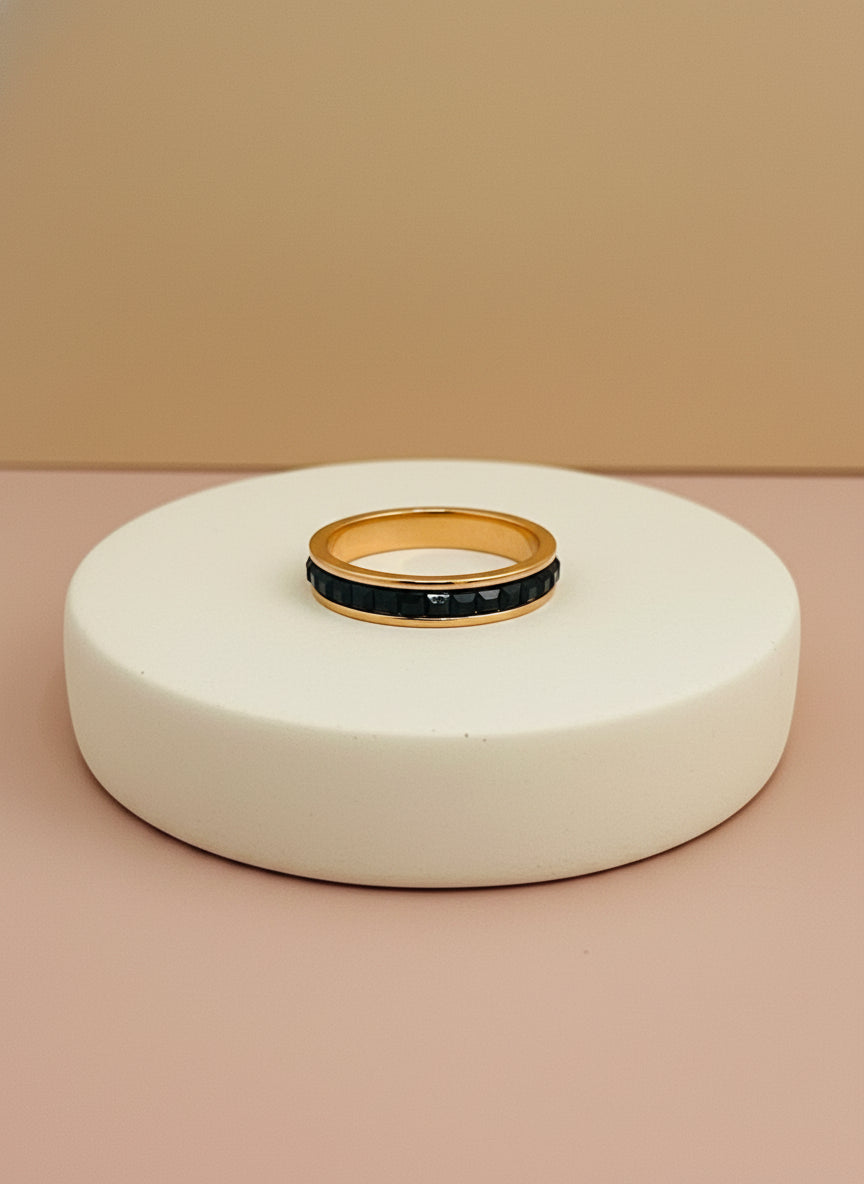 Rose Gold ring with black stones on a white box with beige background