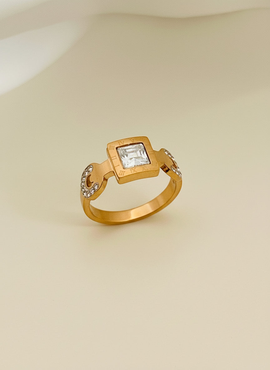 Rose Gold ring with a square gemstone on a white cushion in a gold box.