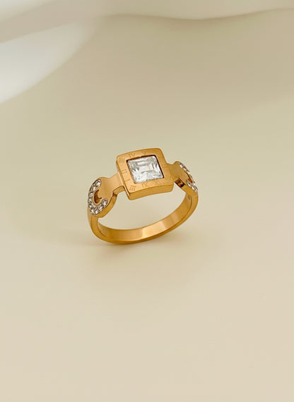 Rose Gold ring with a square gemstone on a white cushion in a gold box.