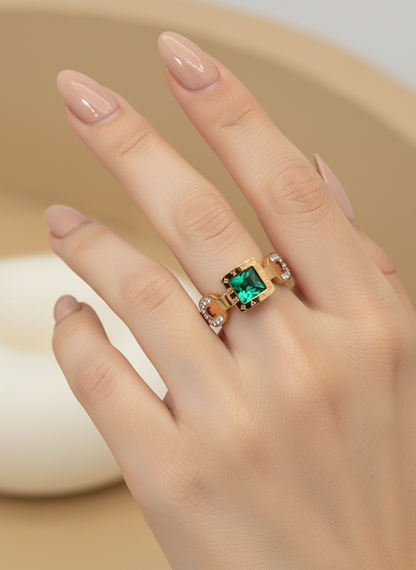 Hand wearing a gold ring with a green gemstone on a neutral background
