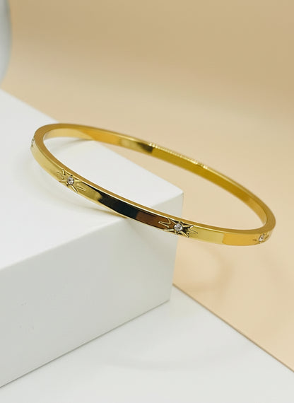 Gold bracelet with engraved design on a wooden block against a white background