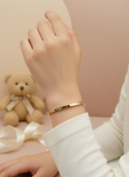 Gold bracelet on a wrist with a teddy bear and ribbon in the background