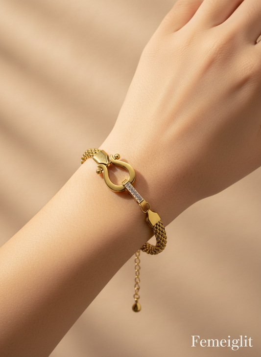 Gold bracelet with a unique design worn on a wrist against a beige background, featuring the brand 'Femeiglit'.
