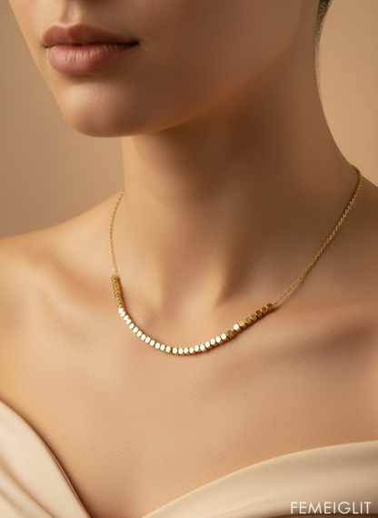 Gold necklace on a model against a beige background with 'FEMEIGLIT' branding.