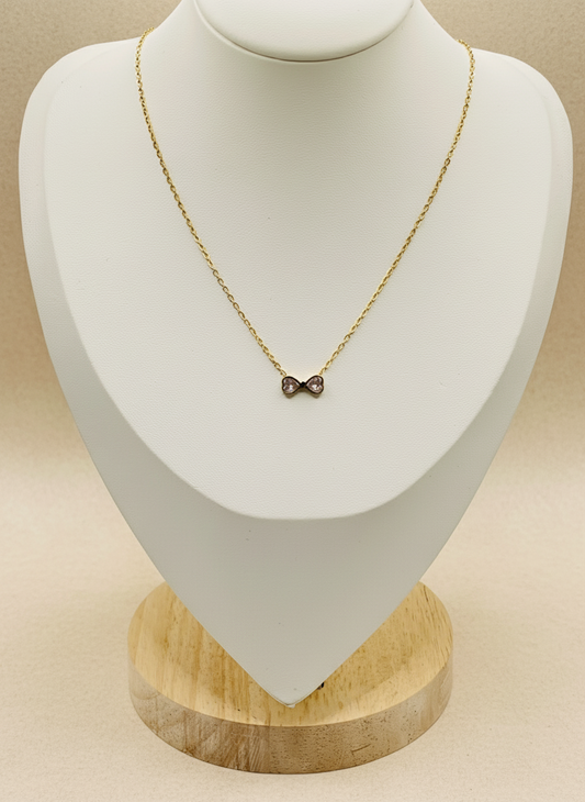 Gold necklace with a bow pendant on a white mannequin bust with a wooden base.