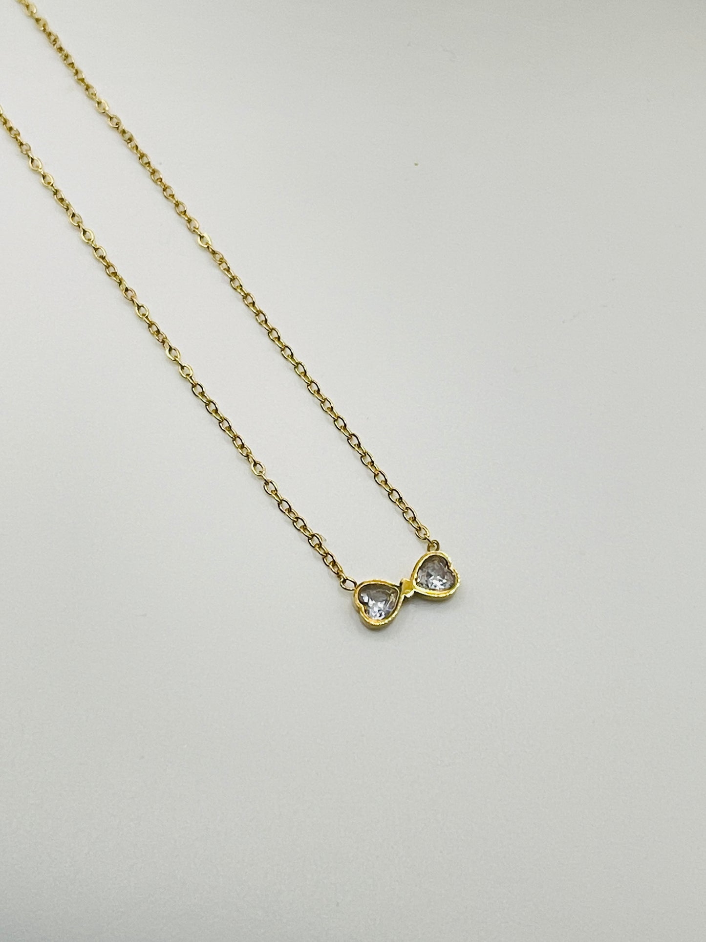 Gold necklace with a heart-shaped pendant on a light gray background