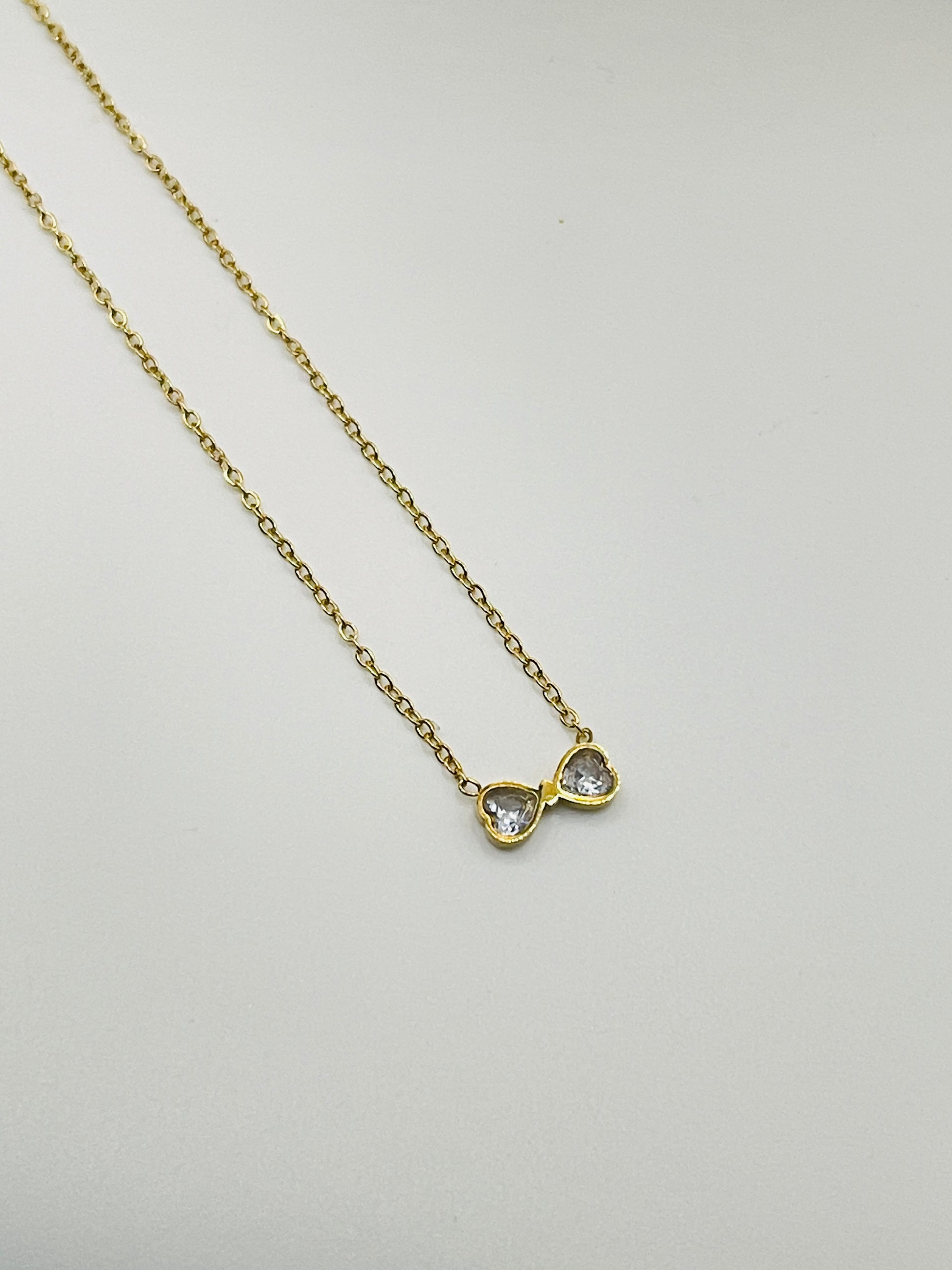 Gold necklace with a heart-shaped pendant on a light gray background