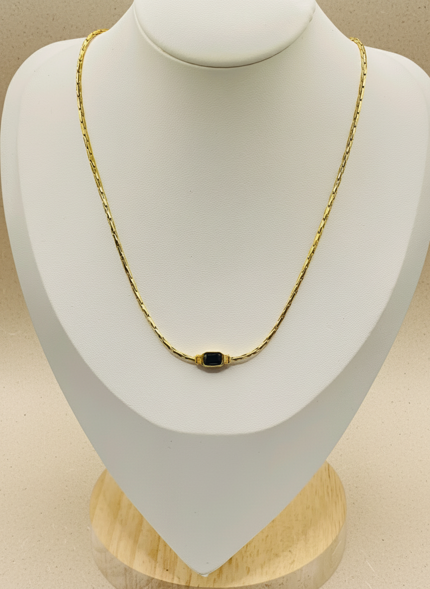 Gold necklace with a black pendant on a mannequin bust.