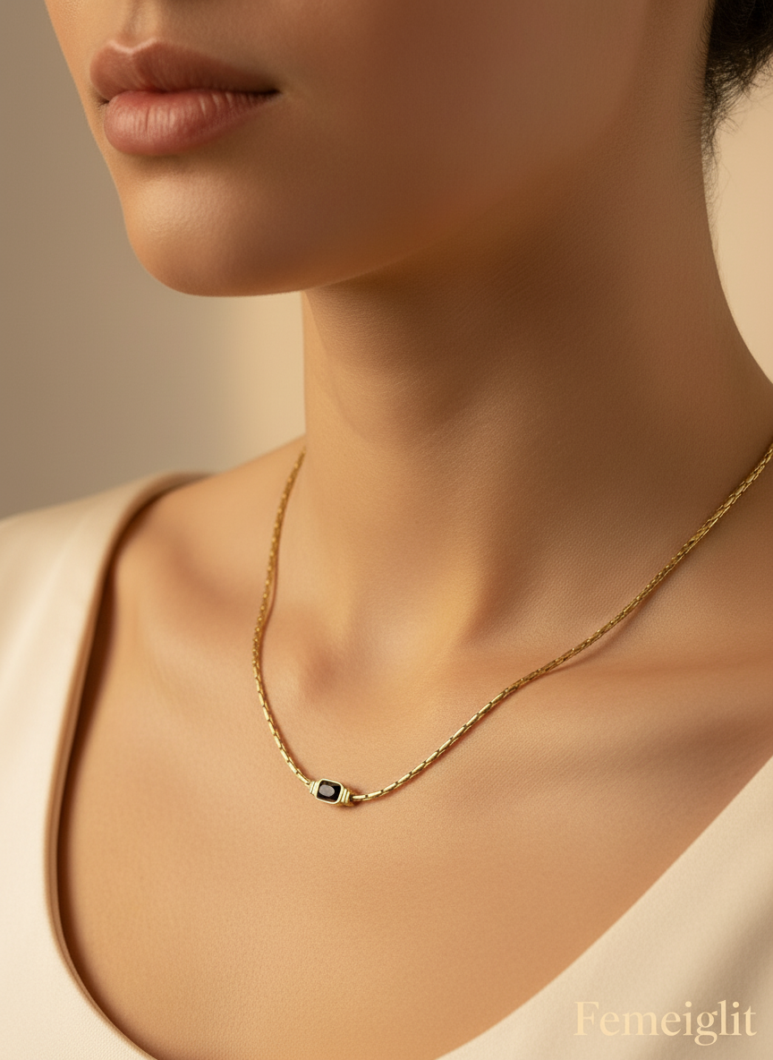 Gold necklace with a black gemstone on a model's neck, branded 'Femeiglit'.