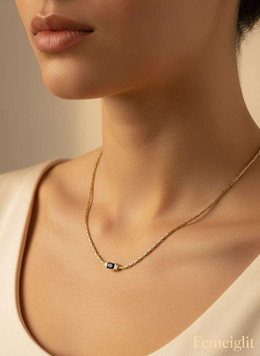 Gold necklace with a black gemstone on a model's neck, branded 'Femeiglit'.