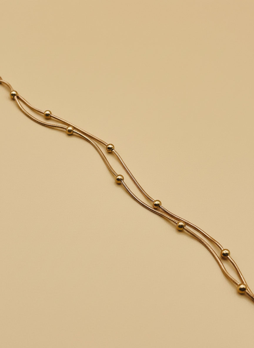 Rose gold chain bracelet on a white surface with a wooden block in the background