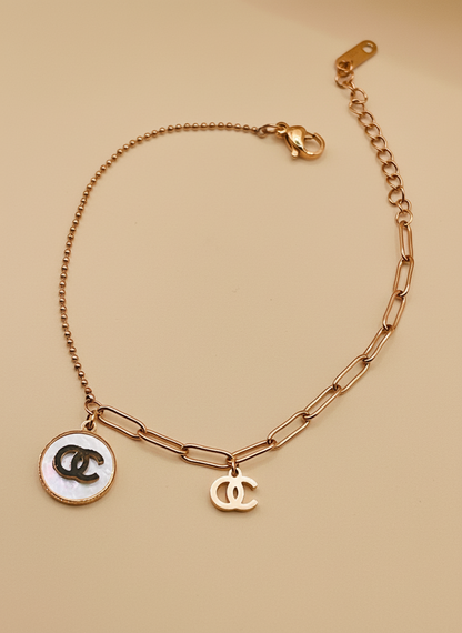 Rose Gold chain bracelet with CC logo charms on a beige background