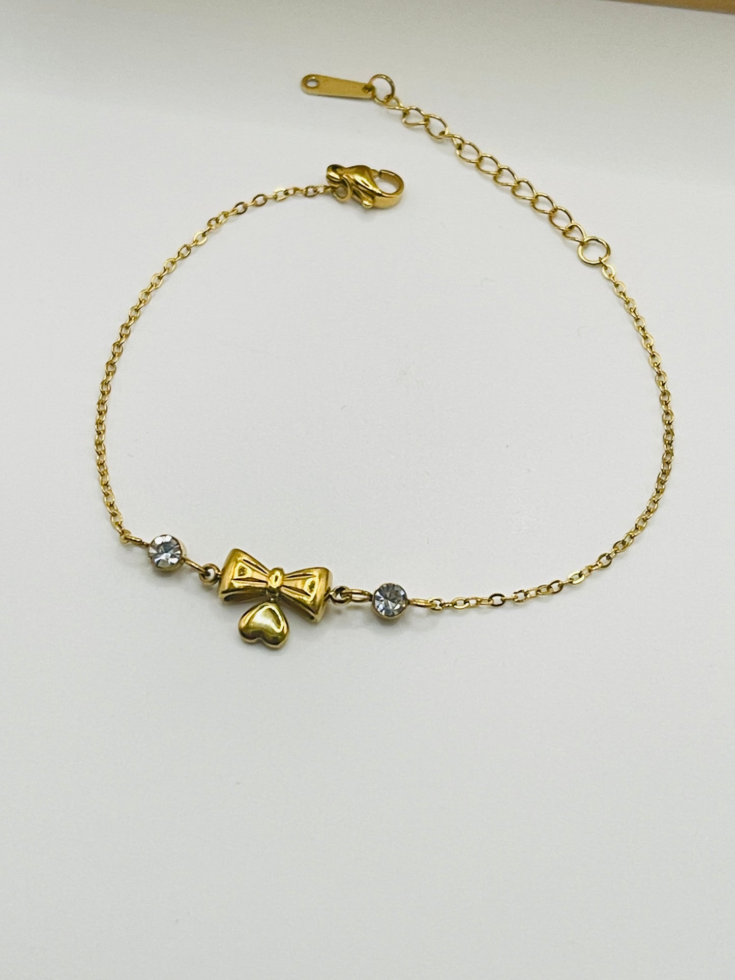 Gold bracelet with bow and heart charm on a white background