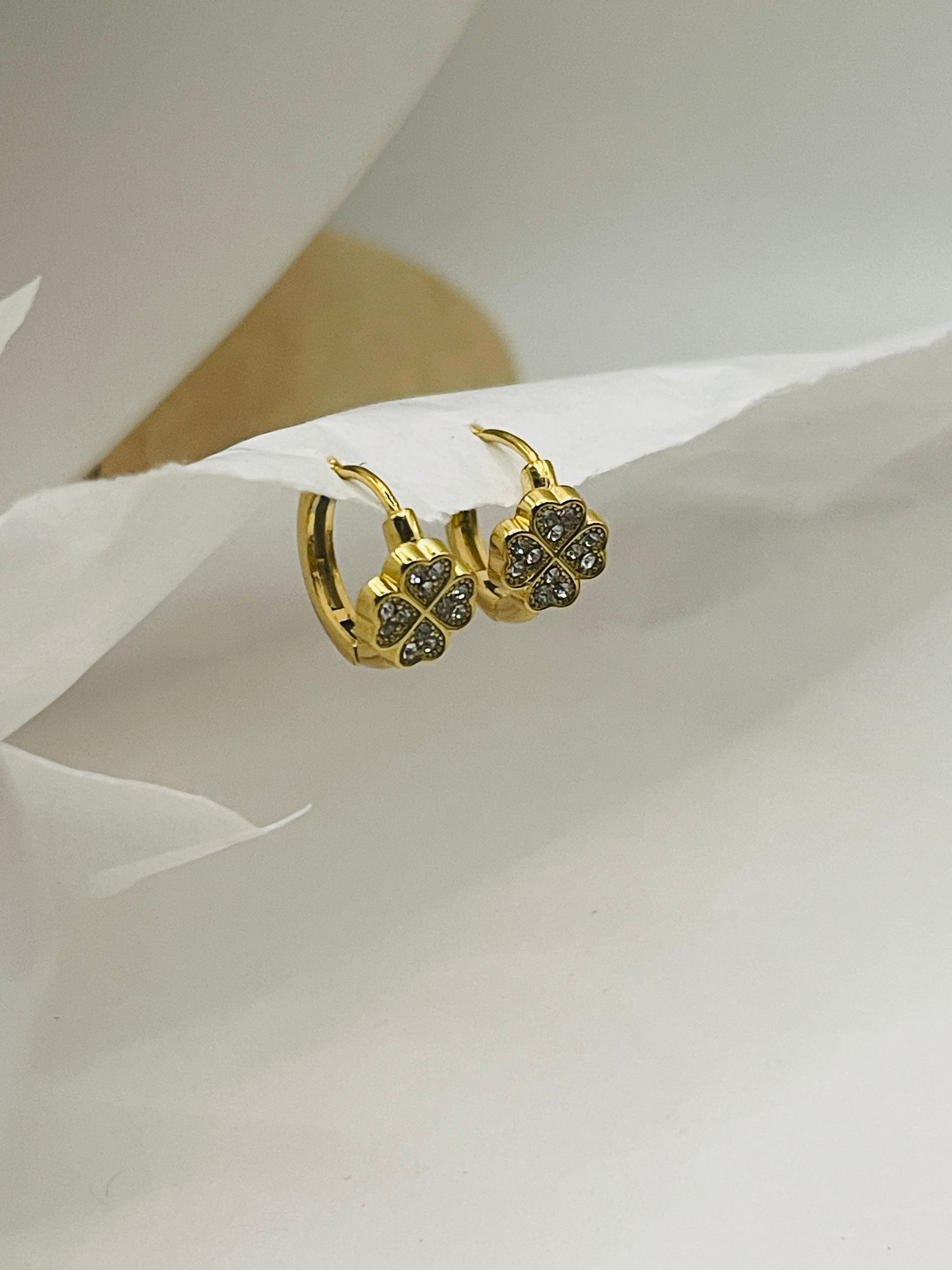 Gold earrings with clover design on a white fabric background