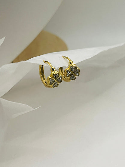 Gold earrings with clover design on a white fabric background