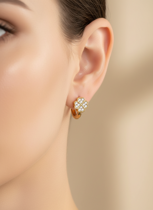 Gold earring with clear stones worn by a model on a beige background