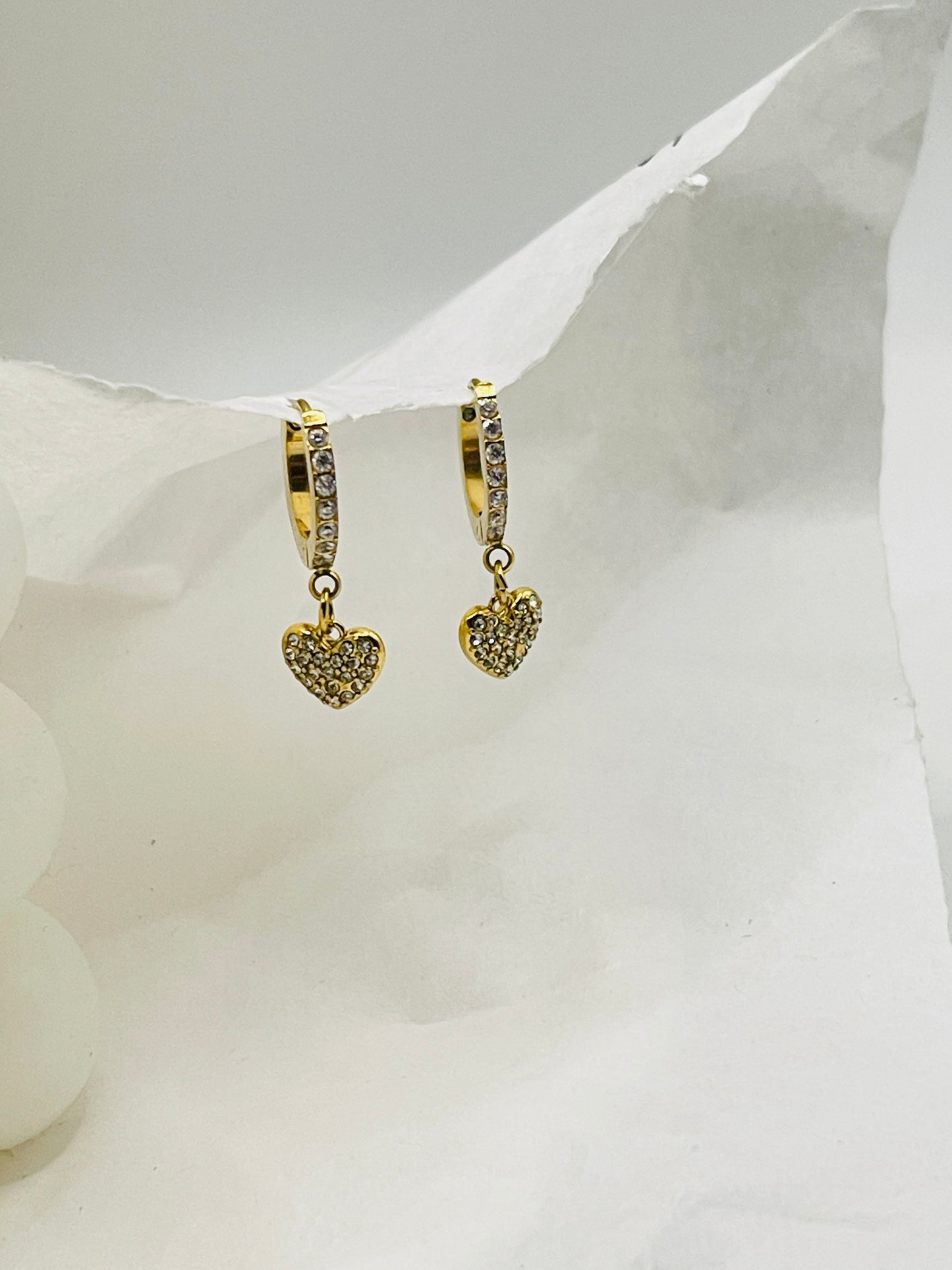 Gold heart-shaped hoop earrings on a white fabric background