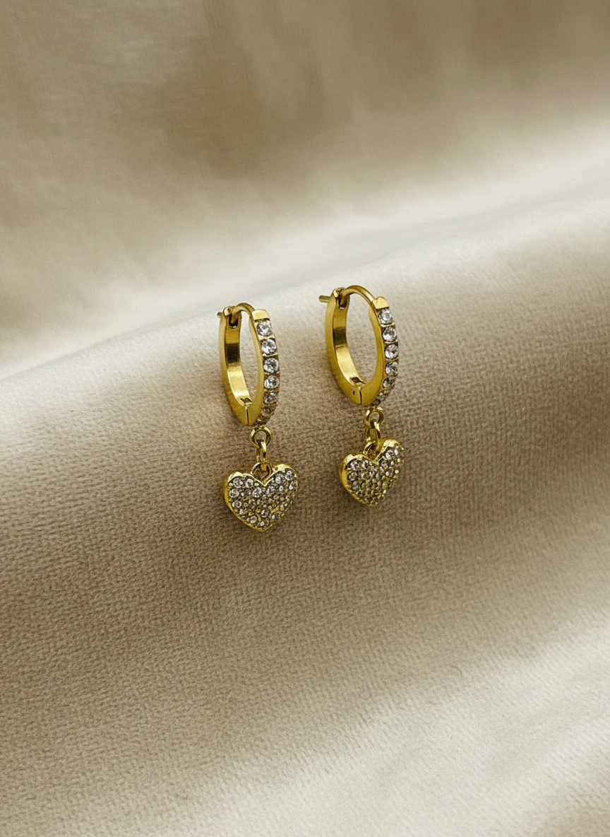 Gold hoop earrings with heart charms on a beige fabric background