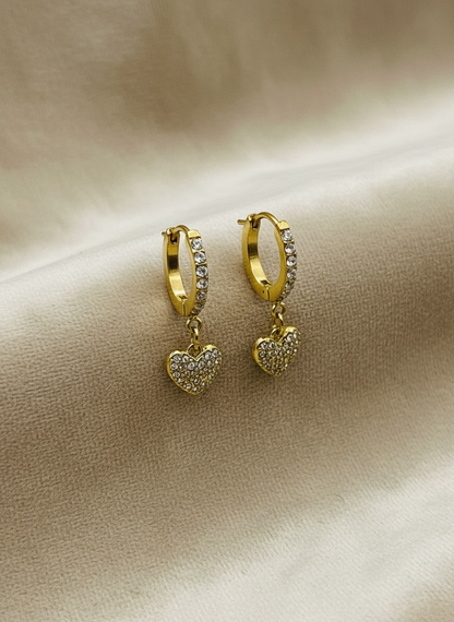 Gold hoop earrings with heart charms on a beige fabric background