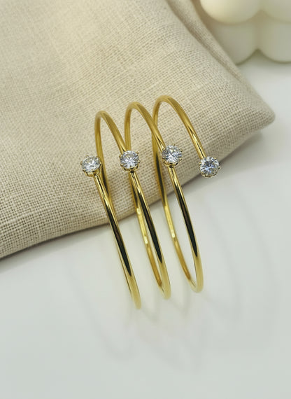 Gold bangles with embedded stones on a soft pink fabric background