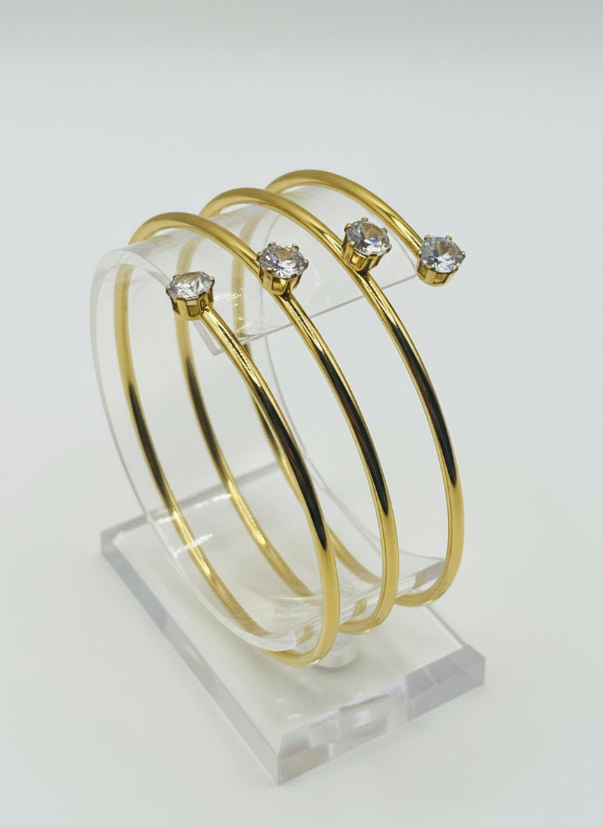 Gold bangles with embedded crystals on a soft pink fabric background