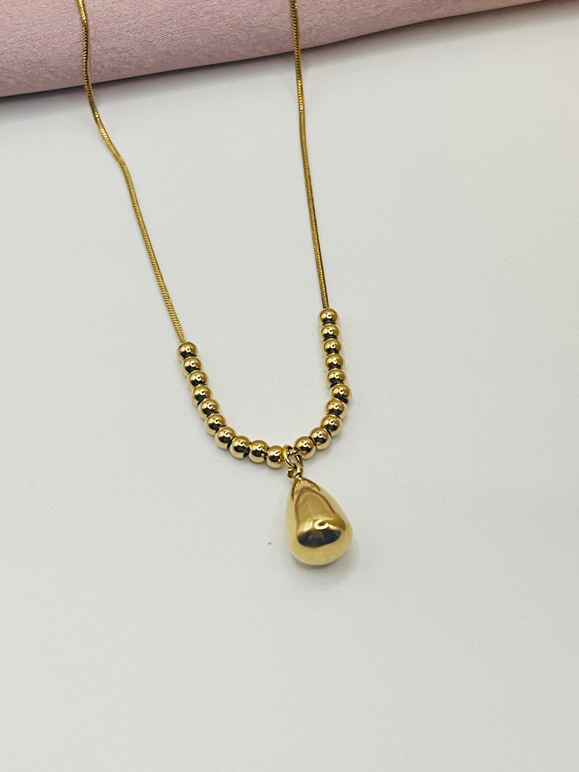 Gold necklace with a heart-shaped pendant on a light pink background