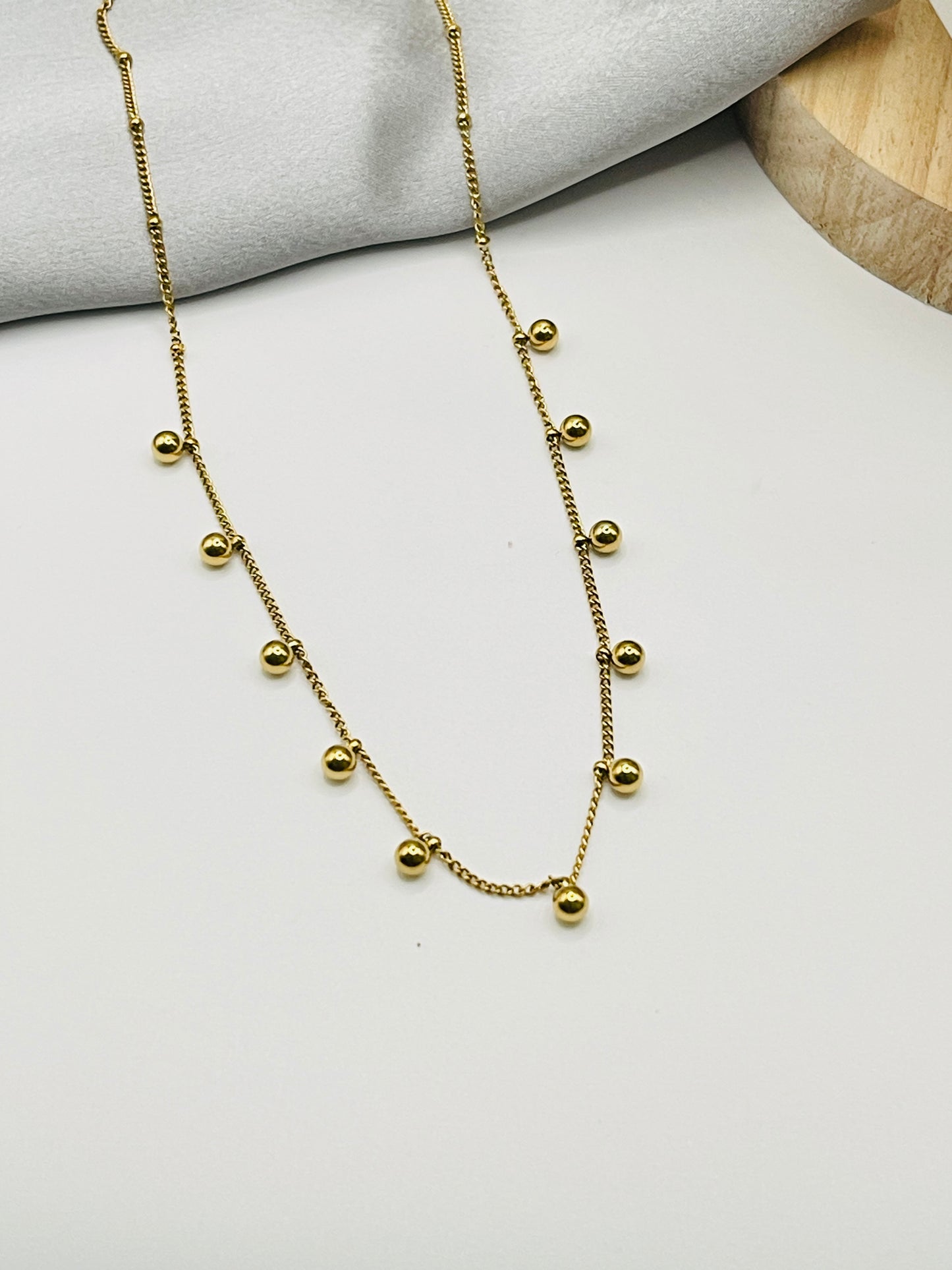 Gold necklace with small beads on a light gray surface