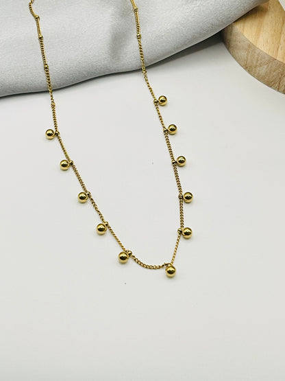 Gold necklace with small beads on a light gray surface