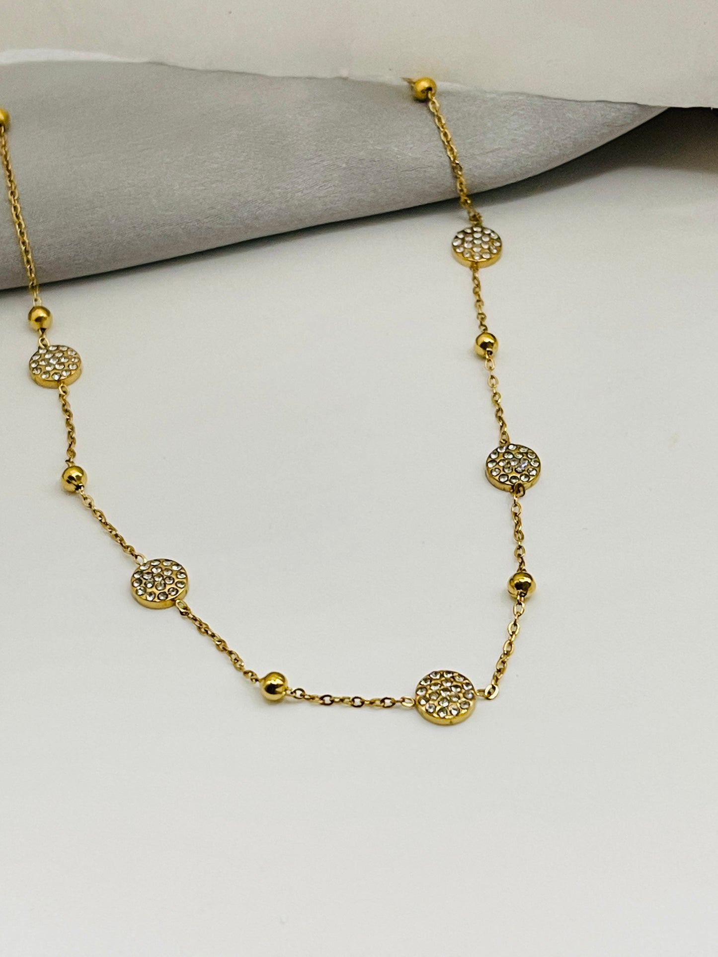 Gold necklace with decorative beads on a light gray surface