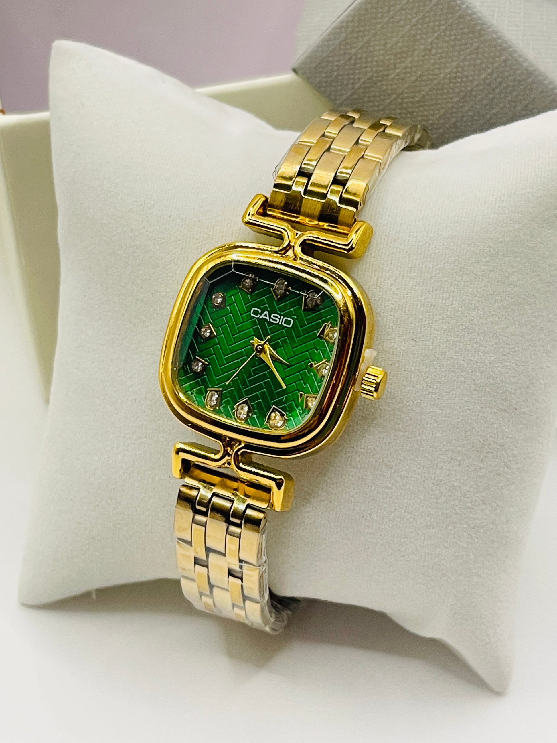 Gold Casio watch with green face on a white cushion