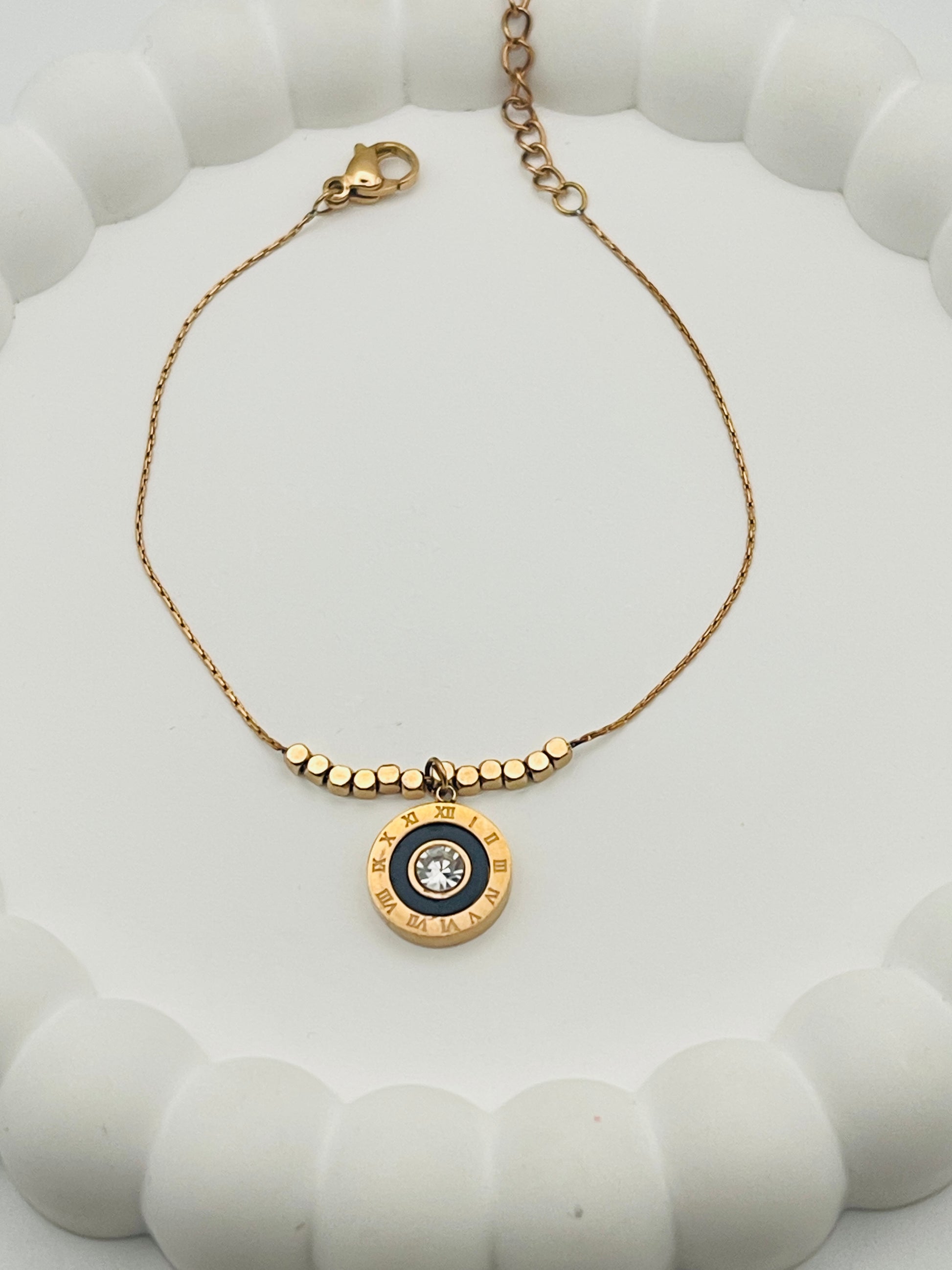 Rose Gold bracelet with a circular pendant on a white textured surface