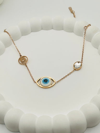 Rose gold bracelet with eye-shaped pendant on a white textured surface
