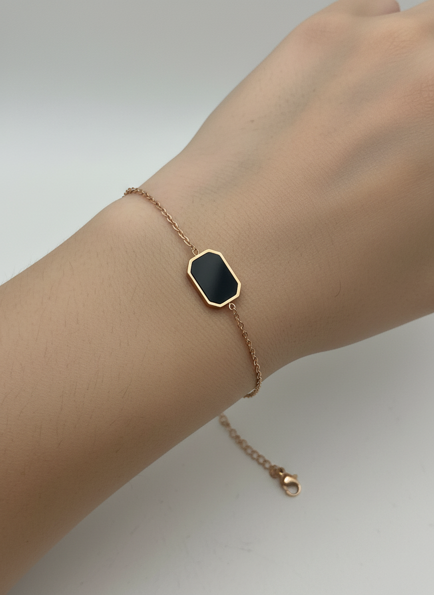 Rose gold bracelet with a black hexagonal charm on a white textured surface