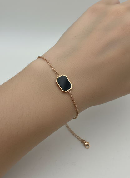 Rose gold bracelet with a black hexagonal charm on a white textured surface