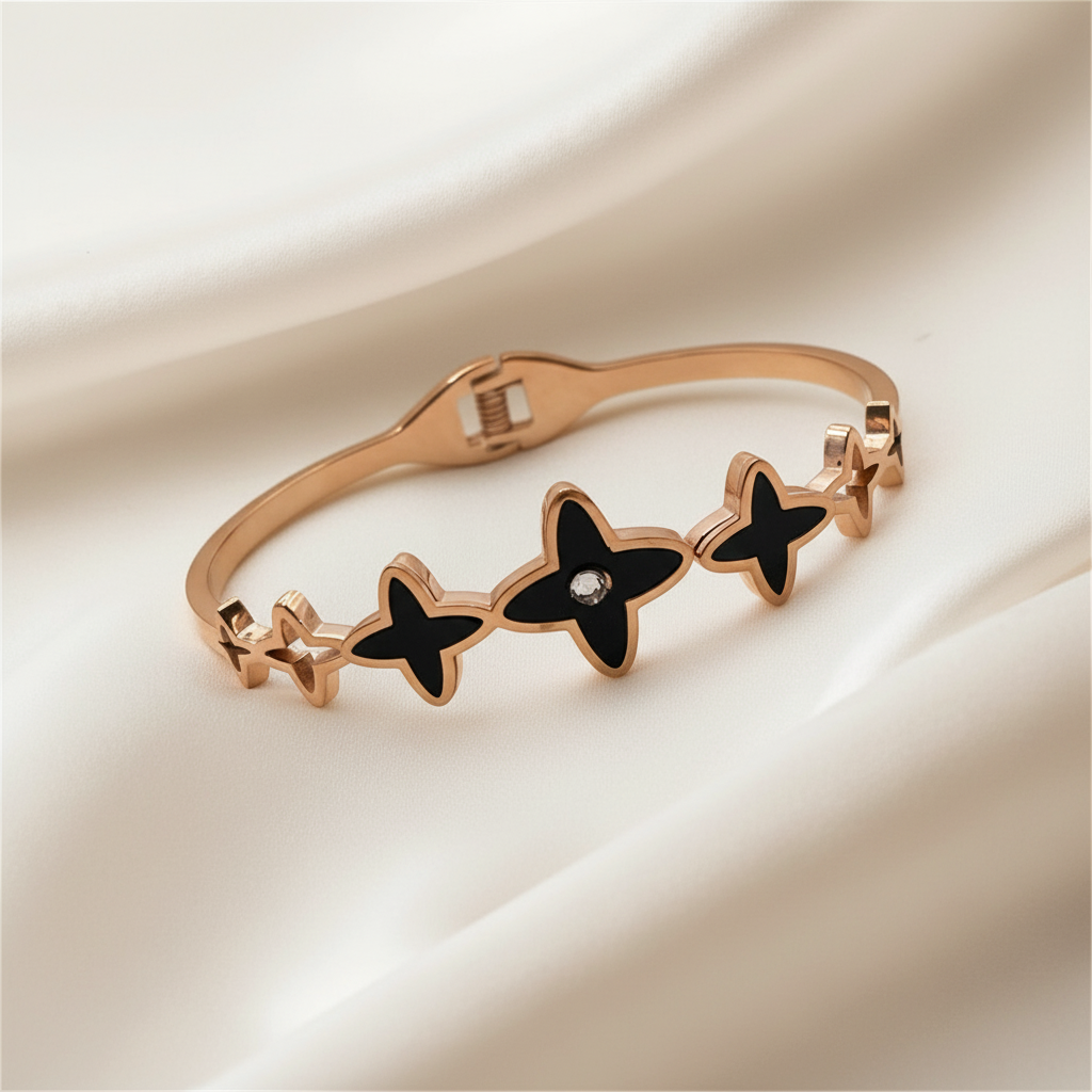 Rose gold bracelet with black star-shaped charms on a beige fabric background