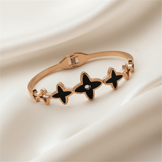 Rose gold bracelet with black star-shaped charms on a beige fabric background