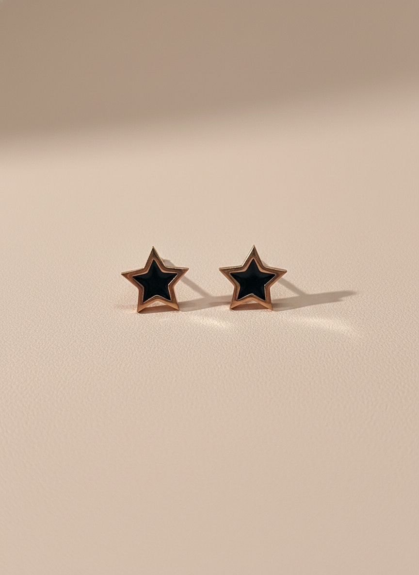 Star-shaped rose gold stud earrings with black centers on a beige background